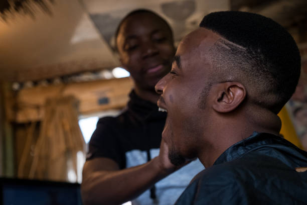 Cleanup after barber has cut my hair A young black male has his hair cut at the local barber shop in the township in Cape Town, South Africa Combing stock pictures, royalty-free photos & images