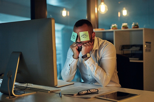 Shot of a tired young businessman working late in an office with sticky notes covering his eyes