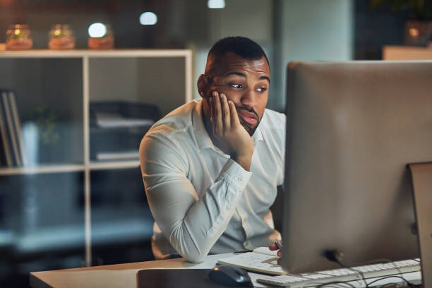 Staring at the screen but nothing's going in Shot of a young businessman looking bored while working at his desk during late night at work dillydally stock pictures, royalty-free photos & images