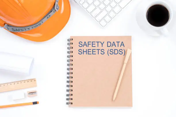 Concept SAFETY DATA SHEETS (SDS). Top viwe of modern workplace with safety helmet, office supplies, a cup of coffee and keyboard on white background. Safety & Health.
