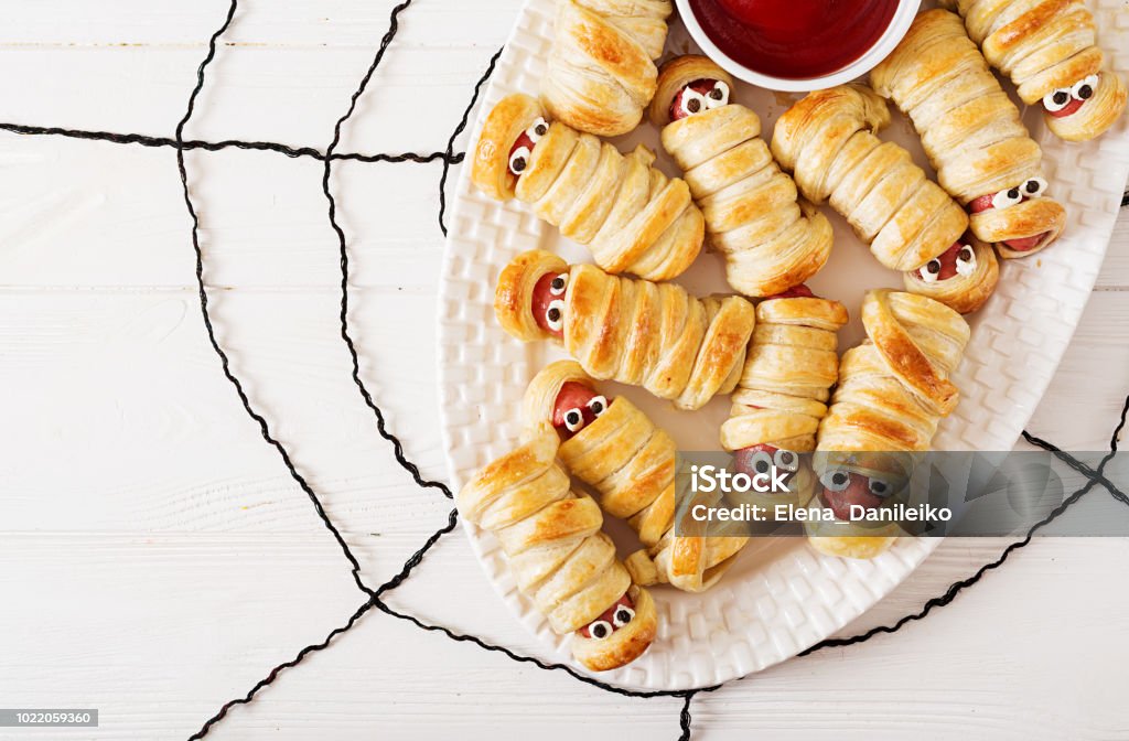 Momias de salchicha miedo en masa con ojos divertidos sobre mesa. Decoración divertida. Comida de Halloween. Vista superior. Endecha plana - Foto de stock de Halloween libre de derechos