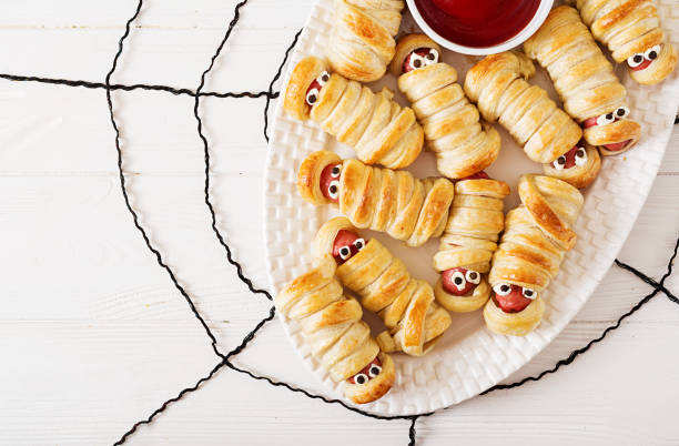 Scary sausage mummies in dough with funny eyes on table. Funny decoration. Halloween food. Top view. Flat lay stock photo