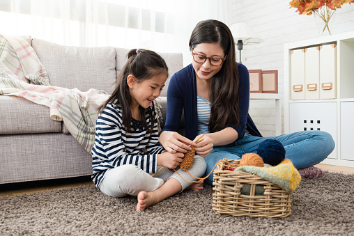 beautiful Asian mom teaches her daughter how to knitting for the autumn sweater for cold season is coming in the living room at home