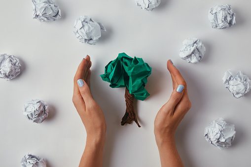 cropped shot of woman covering crumpled papers in shape of tree on white surface