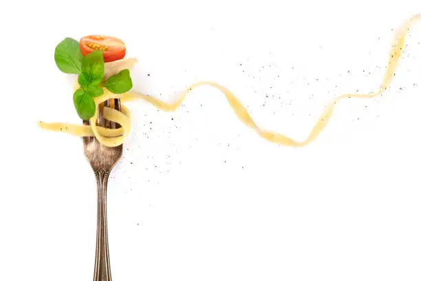 Photo of Italian pasta. Overhead photo of vintage fork with pappardelle, basil, cheese, and tomato, on white background