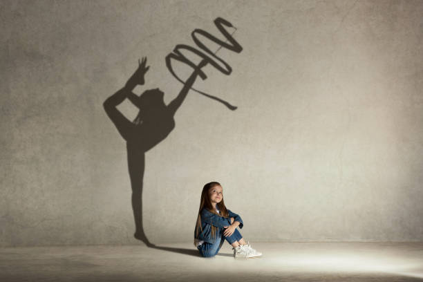 Baby girl dreaming about gymnast profession. Childhood concept Baby girl dreaming about gymnast profession. Childhood and dream concept. Conceptual image with shadow of female gymnast on the studio wall rhythm photos stock pictures, royalty-free photos & images