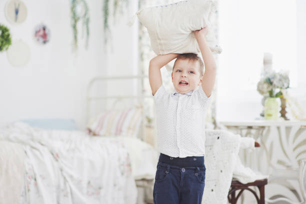 kleiner junge im weißen hemd mit kissen. kissenschlacht - furniture barefoot little boys family stock-fotos und bilder