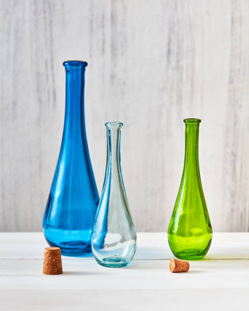 Three multicolored glass bottles with stoppers for saving olive oil on a gray background, a table