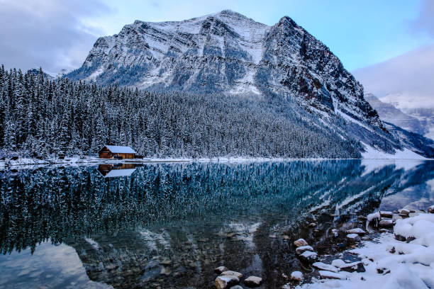 Log hut on the Lake Louise, Canada The Canadian Rockies in October, mountain range dusted in first snow, cloudy, morning light. small wooden hut on the other side of the lake. Reflection on the water in the foreground winter sunrise mountain snow stock pictures, royalty-free photos & images