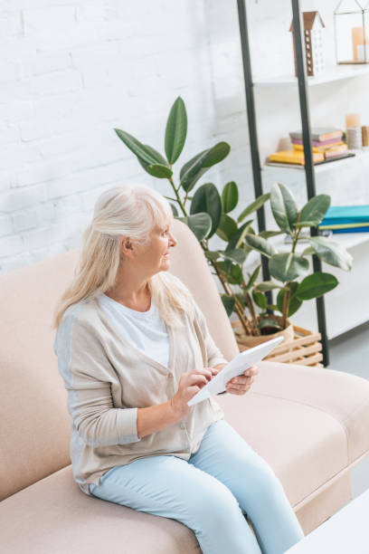 istock high angle view of smiling senior woman using digital tablet while sitting on couch 1022113336
