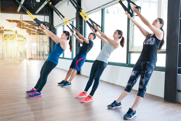 group of fitness TRX suspension straps training group of fitness TRX suspension straps training exercises Asian people doing the pull up, working with own weight in a sunny bright gym. suspension training stock pictures, royalty-free photos & images