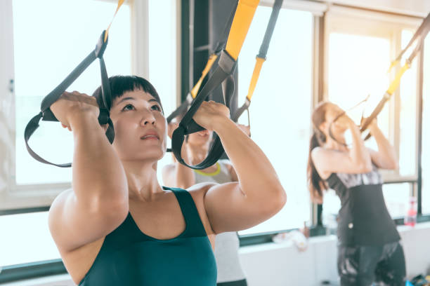 strong woman using her muscle to pull up strong Asian woman using her muscle to pull up with her body training with TRX fitness system. suspension training stock pictures, royalty-free photos & images