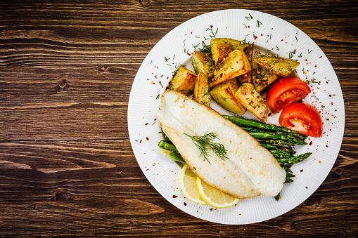 Fried fish fillet with fried potatoes and vegetables served on wooden table