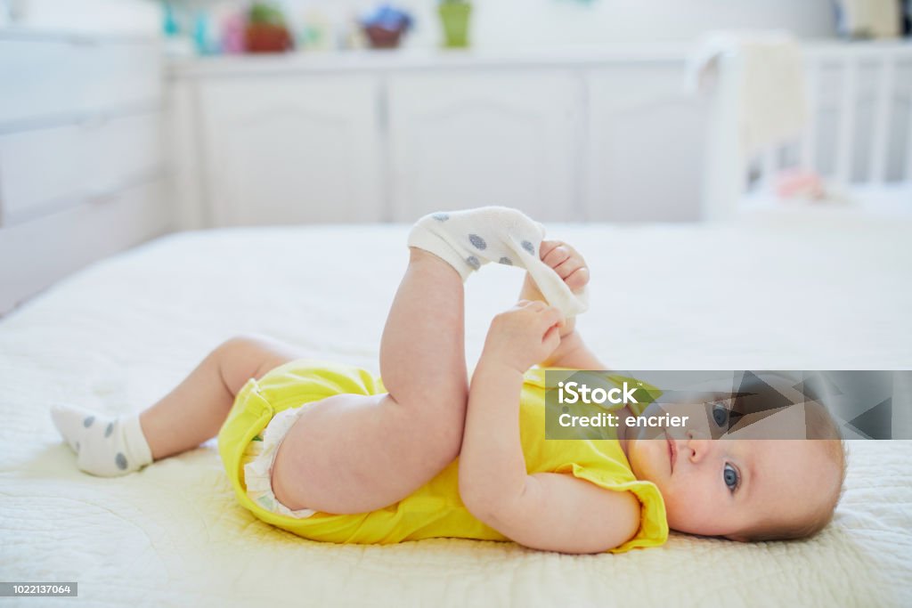 Adorable baby girl removing sock from her foot Adorable baby girl removing sock from her foot. Little child having fun. Infant kid in sunny nursery Baby Girls Stock Photo