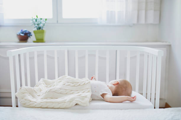Baby girl sleeping in co-sleeper crib Adorable baby girl sleeping in co-sleeper crib attached to parents' bed. Little child having a day nap in cot. Infant kid in sunny nursery rodent bedding stock pictures, royalty-free photos & images