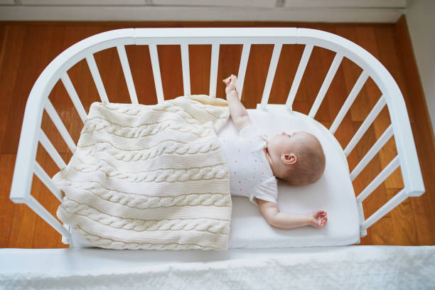 Baby girl sleeping in co-sleeper crib Adorable baby girl sleeping in co-sleeper crib attached to parents' bed. Little child having a day nap in cot. Infant kid in sunny nursery sidecar photos stock pictures, royalty-free photos & images