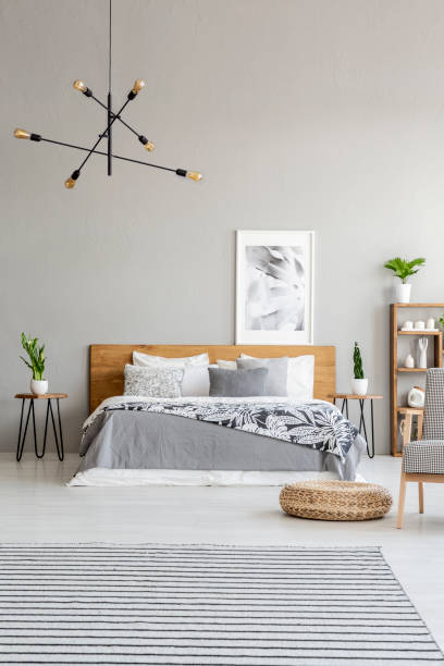 istock Patterned carpet and pouf in spacious grey bedroom interior with poster above wooden bed. Real photo 1022138156