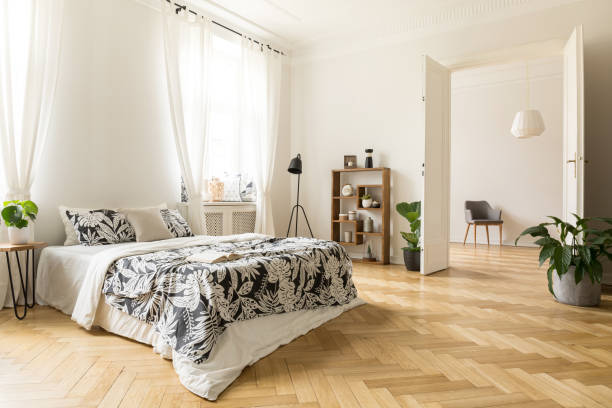 Stylish apartment interior with white walls and herringbone wooden floor. A view from a bedroom with a big bed to another room with an armchair. Real photo. Stylish apartment interior with white walls and herringbone wooden floor. A view from a bedroom with a big bed to another room with an armchair. Real photo. building story photos stock pictures, royalty-free photos & images