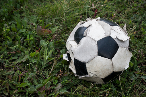 Old black and white soccer ball (Football) on green grass