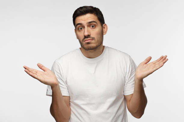 istock I don't know. Young man isolated on grey background being at a loss, showing helpless gesture with arm and hands, mouth curved as if he does not know what to do 1022174614