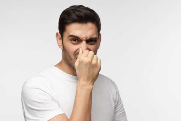 porträt von schönen jungen mann in freizeitkleidung isoliert auf grauem hintergrund hält seine nase, als ob etwas faul und stinkenden suchen beiseite suche nach quelle der geruch riechen - facial expression unpleasant smell shirt caucasian stock-fotos und bilder