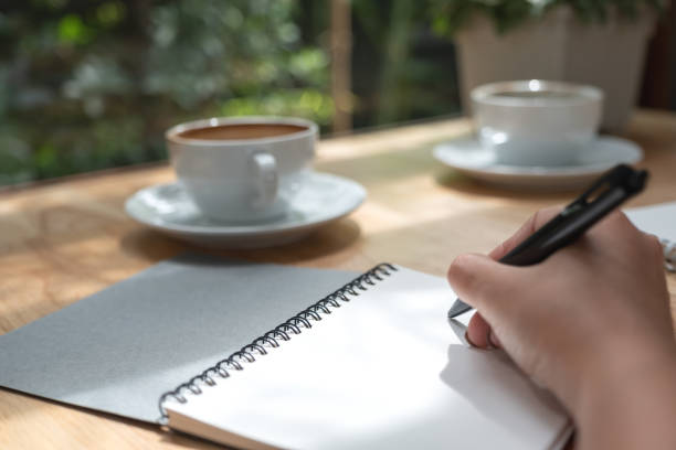 istock Closeup image of a hand writing down on a white blank notebook with coffee cup on wooden table 1022181844