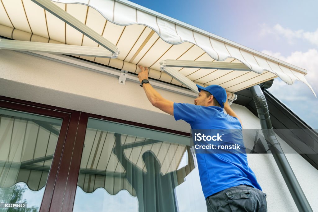 worker install an awning on the house wall over the terrace window Awning Stock Photo