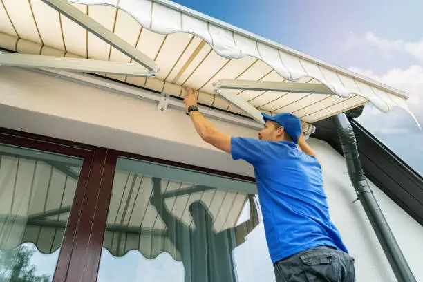 Photo of worker install an awning on the house wall over the terrace window