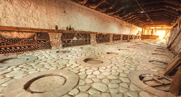 Huge stone cellar with aged dust wine bottles and qvevri, large earthenware vessels under ground. Rustic farmhouse interior with rural storage of winery