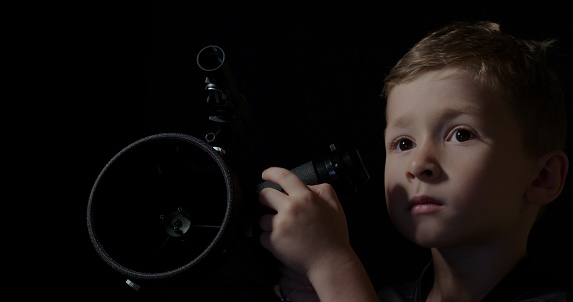 A boy looking through a astronomy telescope.