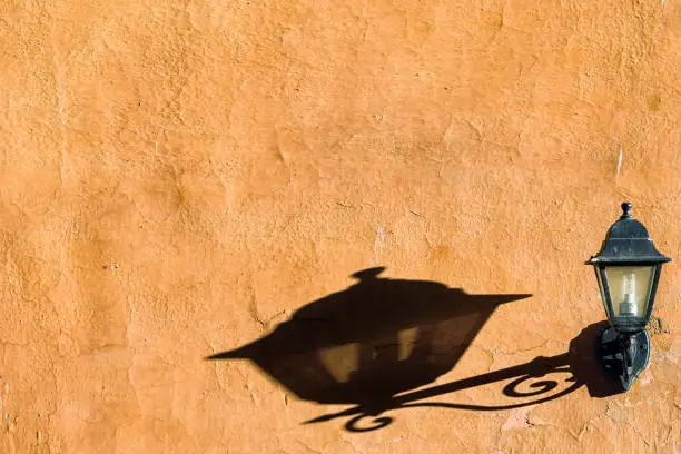 Black metal street lamp and detailed shadow on sand coloured rendered wall in Italy