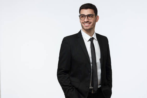 half-length picture of handsome caucasian businessman isolated on gray background wearing black suit and eyeglasses looking aside with happy smile, looking relaxed and full of ideas and ambitions - half smile imagens e fotografias de stock