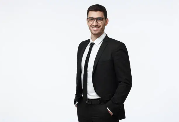 Photo of Indoor picture of young business man in glasses pictured isolated on grey background looking straight at camera, showing confidence and providing stability for employees