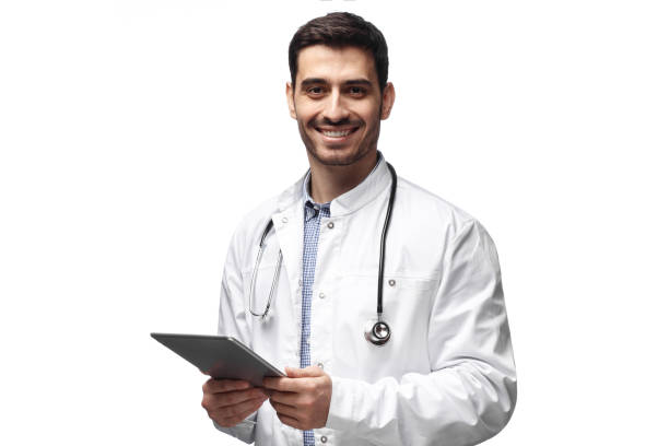 Handsome man doctor standing isolated in white background holding tablet device, showing confidence and optimism while giving straight open look and smiling Handsome man doctor standing isolated in white background holding tablet device, showing confidence and optimism while giving straight open look and smiling paramedic photos stock pictures, royalty-free photos & images