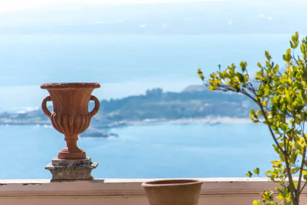 View to the sea coast from a balcony in Taormina, Italy, with an amphora visible in the foreground