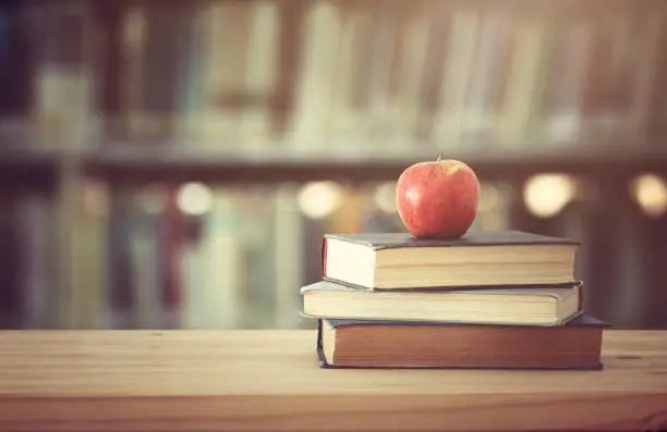 Photo of back to school concept. stack of books over wooden desk in front of library and shelves with books.