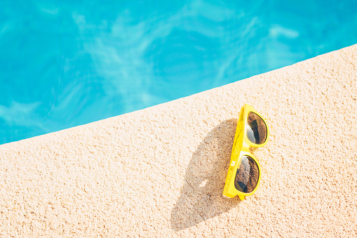 Yellow sunglasses on the edge of the pool on a bright sunny summer day, vacations by the sea