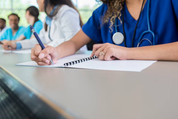 Unrecognizable medical student writes in class workbook An unrecognizable medical student sits at a table in her lecture hall and writes in her class workbook. medical student photos stock pictures, royalty-free photos & images