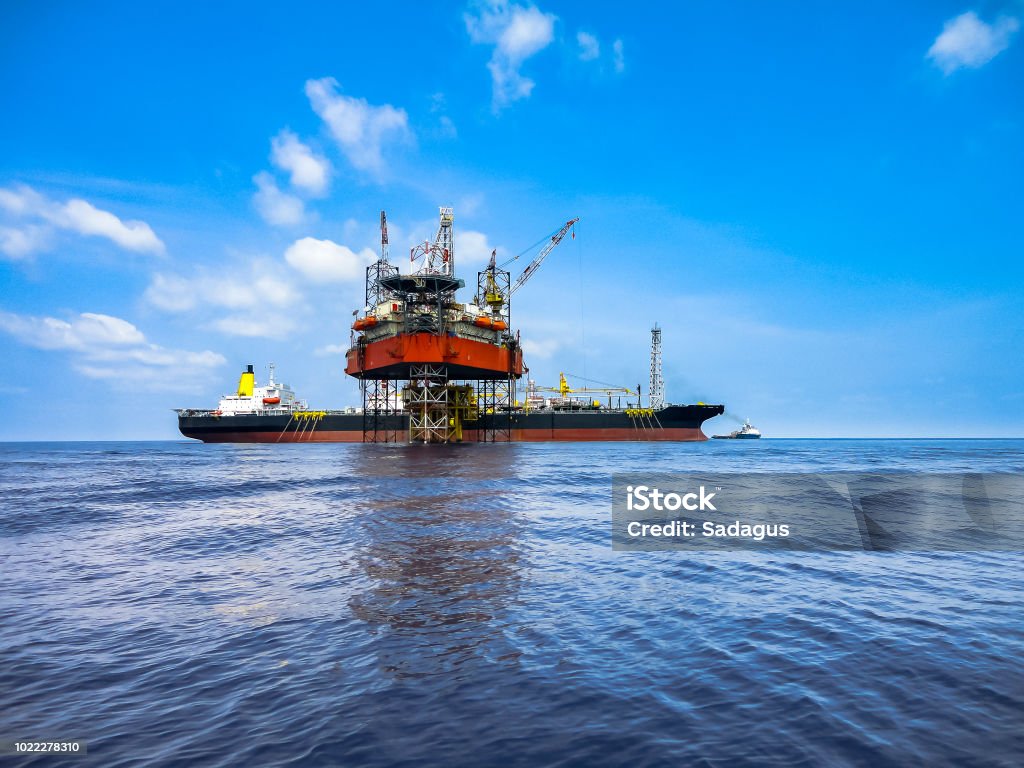 Jack up drilling rig and FPSO ship in oil field Jack up drilling rig on oil well platform with FPSO ship on site with beautiful cloudy blue sky in offshore oil field Floating On Water Stock Photo