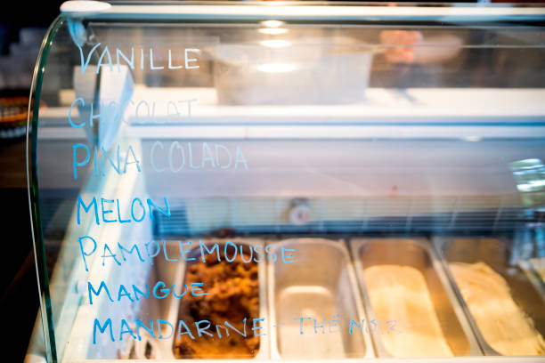 Customer service in a small artisanal ice cream parlor. Selective focus flavour written in french on the refrigerator door. No people visible. Square indoors waist up shot with copy space.