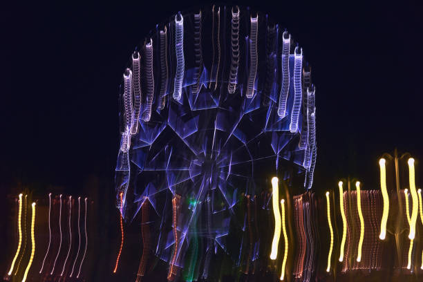 lubrificata quando si sposta la fotocamera su una lunga esposizione illuminata da colori vivaci, la ruota panoramica nel parco crea diversi varini di linee di luce e colori per lo sfondo e i motivi - ferris wheel wheel blurred motion amusement park foto e immagini stock