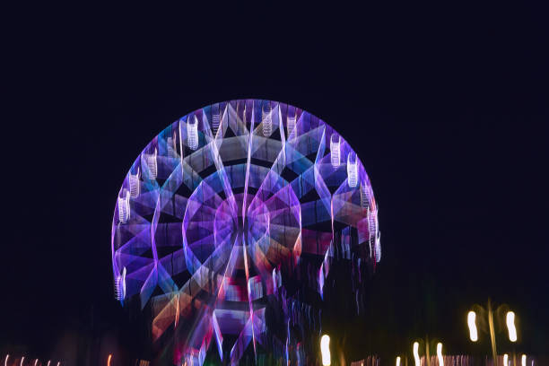lubrificata quando si sposta la fotocamera su una lunga esposizione illuminata da colori vivaci, la ruota panoramica nel parco crea diversi varini di linee di luce e colori per lo sfondo e i motivi - ferris wheel wheel blurred motion amusement park foto e immagini stock