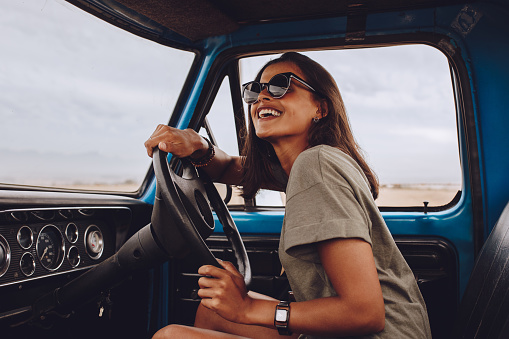 Portrait of happy young woman driving a car and smiling. Beautiful woman going on a road trip on a old truck.