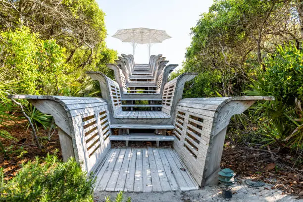 Closeup of wooden pavilion stairs leading to beach ocean with umbrella going up steps in Florida, sand, green shrubs, plants, nobody empty landscape view during sunny day