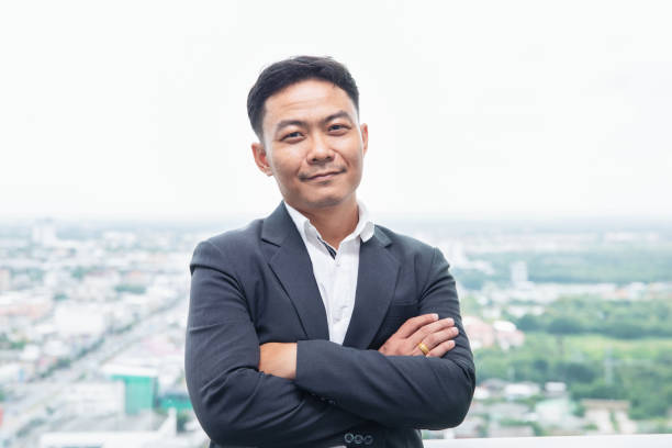 istock smiling asian businessman with arm crossing on skyscraper background 1022362436