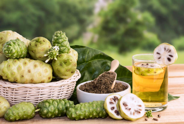 succo di frutta noni o morinda citrifolia con fetta di noni e polvere noni per la salute sullo sfondo di legno con spazio di copia per il testo. - anticancer foto e immagini stock