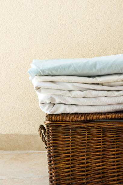 istock Stacked clean folded cotton bedlinen on wicker chest white wall background. Laundry cleanliness concept. Provence Mediterranean nordic interior. Poster banner with copy space 1022372710