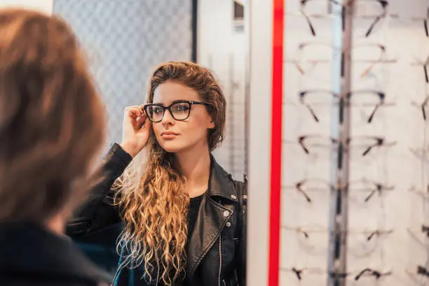Woman trying new glasses, looking on mirror.