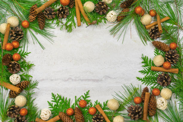 istock A border of cedar, white pine, and hemlock branches along with scotch pine. spruce, and hemlock pine cones, cinnamon sticks, and sparkly orange balls  with copy space in the middle 1022397706