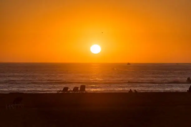 Sunset over Atlantic Ocean, people, seagulls and beachchairs in Agadir Morocco